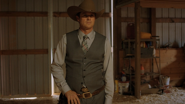 Eric Close, actor, in a cowboy hat and a determined gaze, standing with his hand on his belt in a rustic shed.