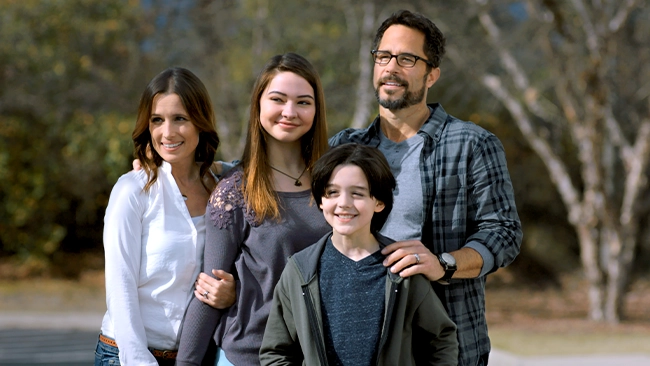Madelyn Cline, Shawn Christian, and Shawnee Smith standing together as a happy family, smiling at something out of frame.